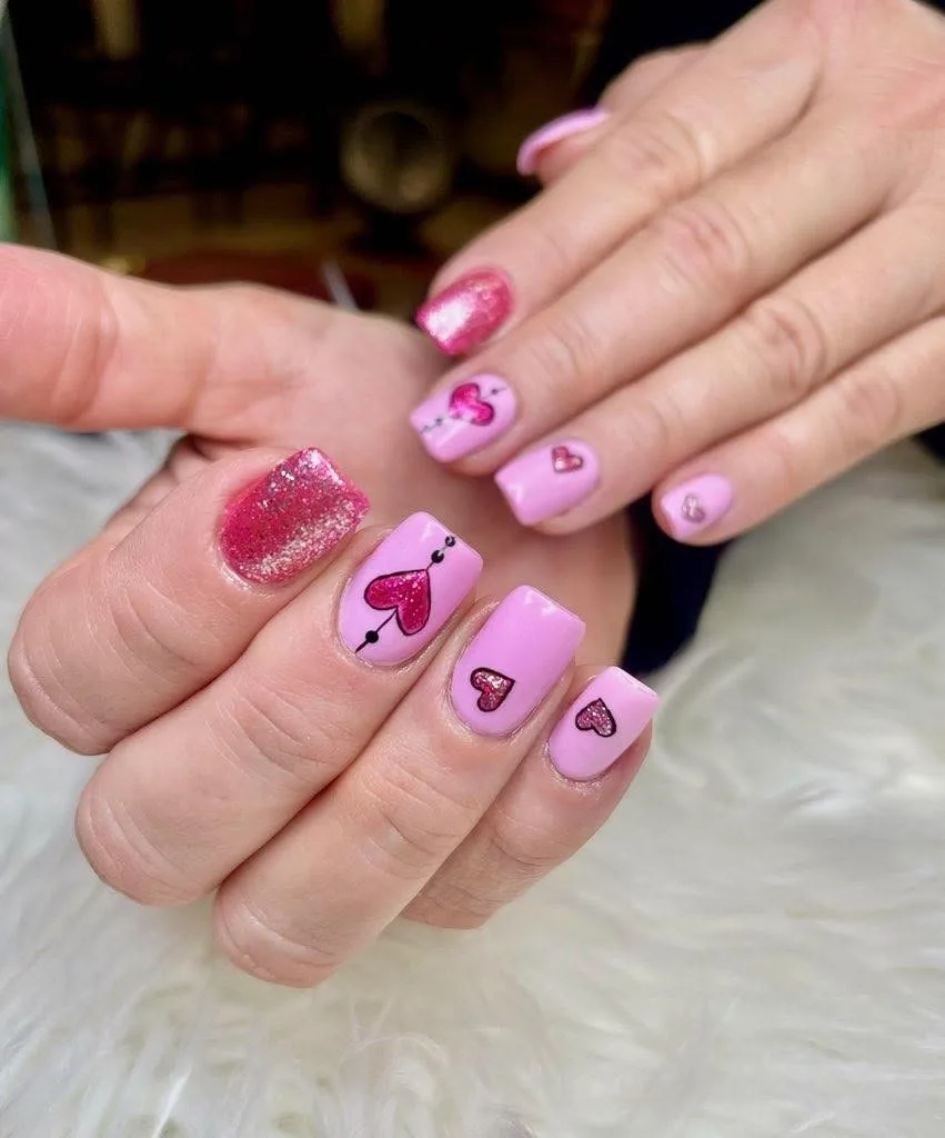 Short pink nails with glitter heart accents.
